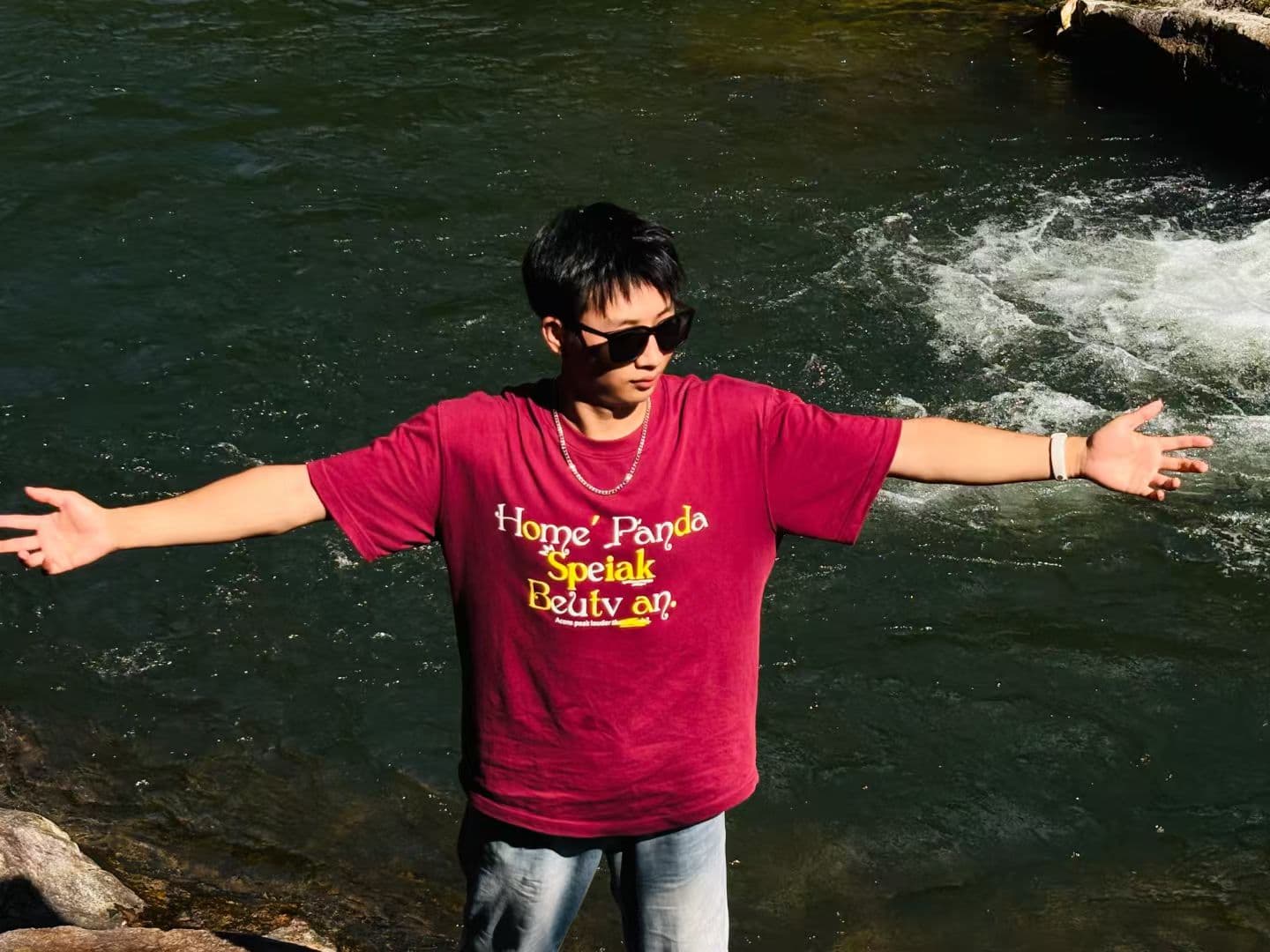 Portrait photo of Yang Chong with arms outstretched beside an outdoor stream